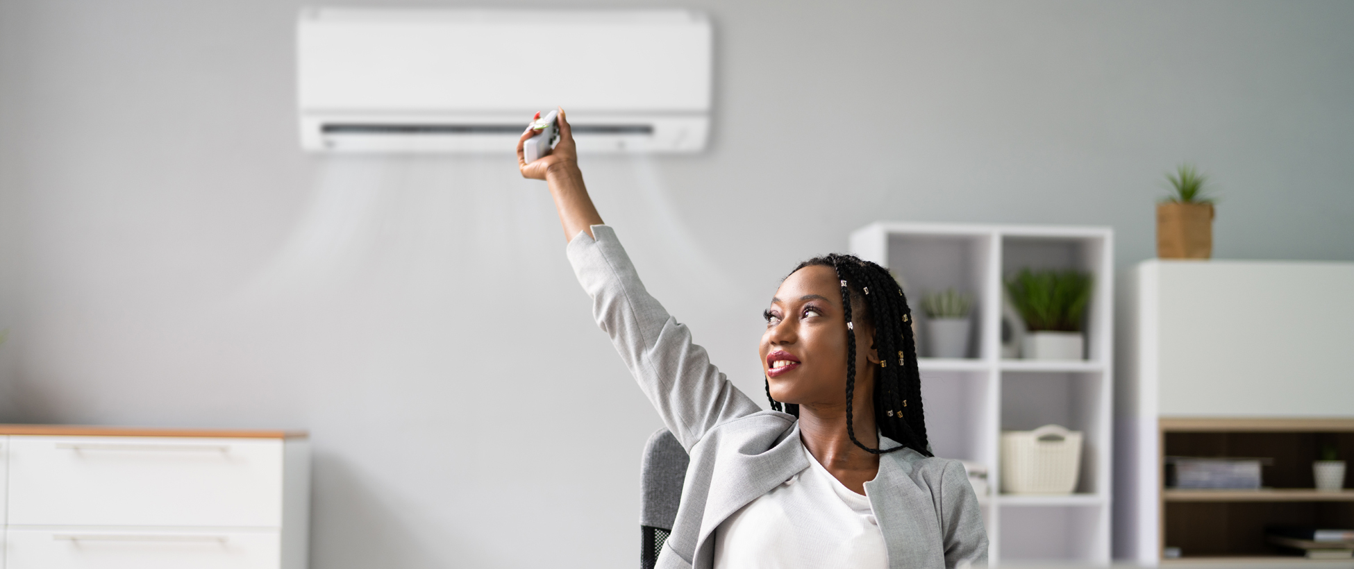 Woman working at her home office desk adjusting the air conditioner unit temperature behind her.