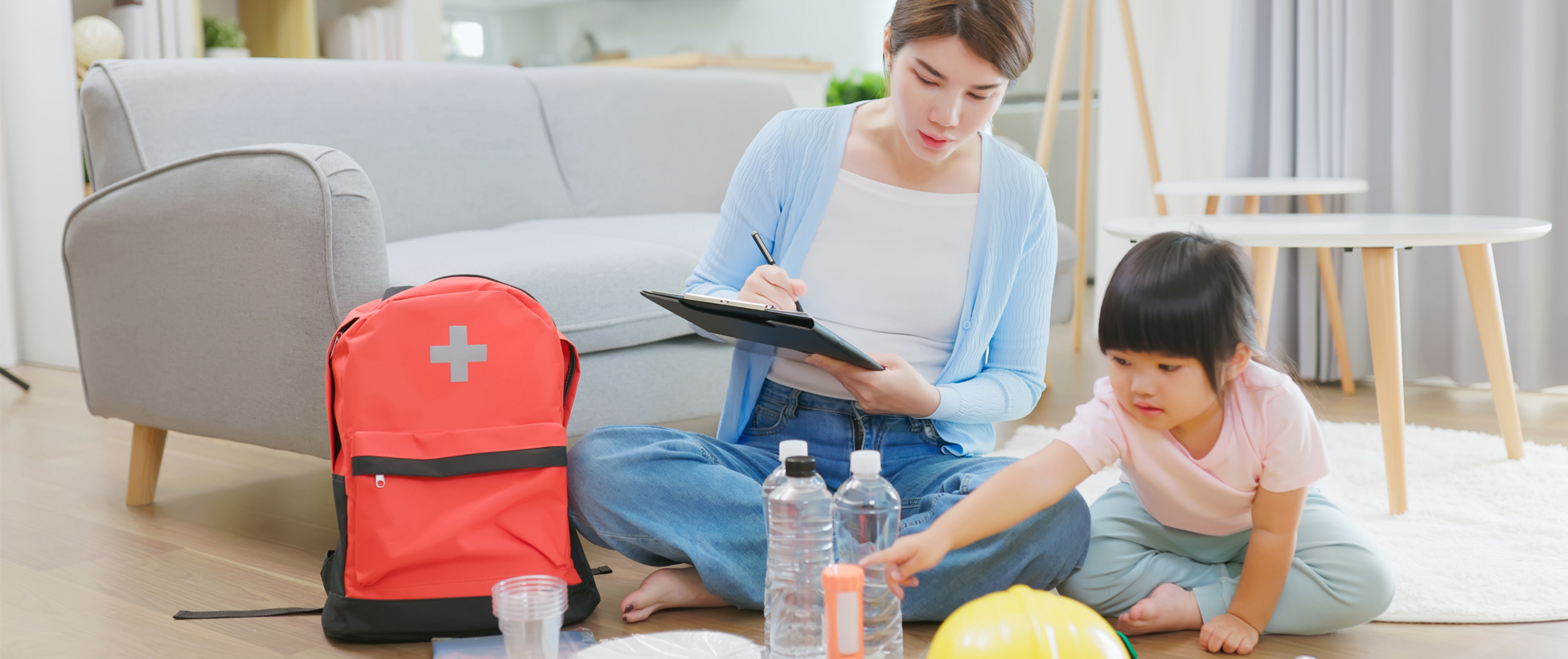 Mother and daughter sitting on the floor of their living room, stocking a family emergency preparedness kit.