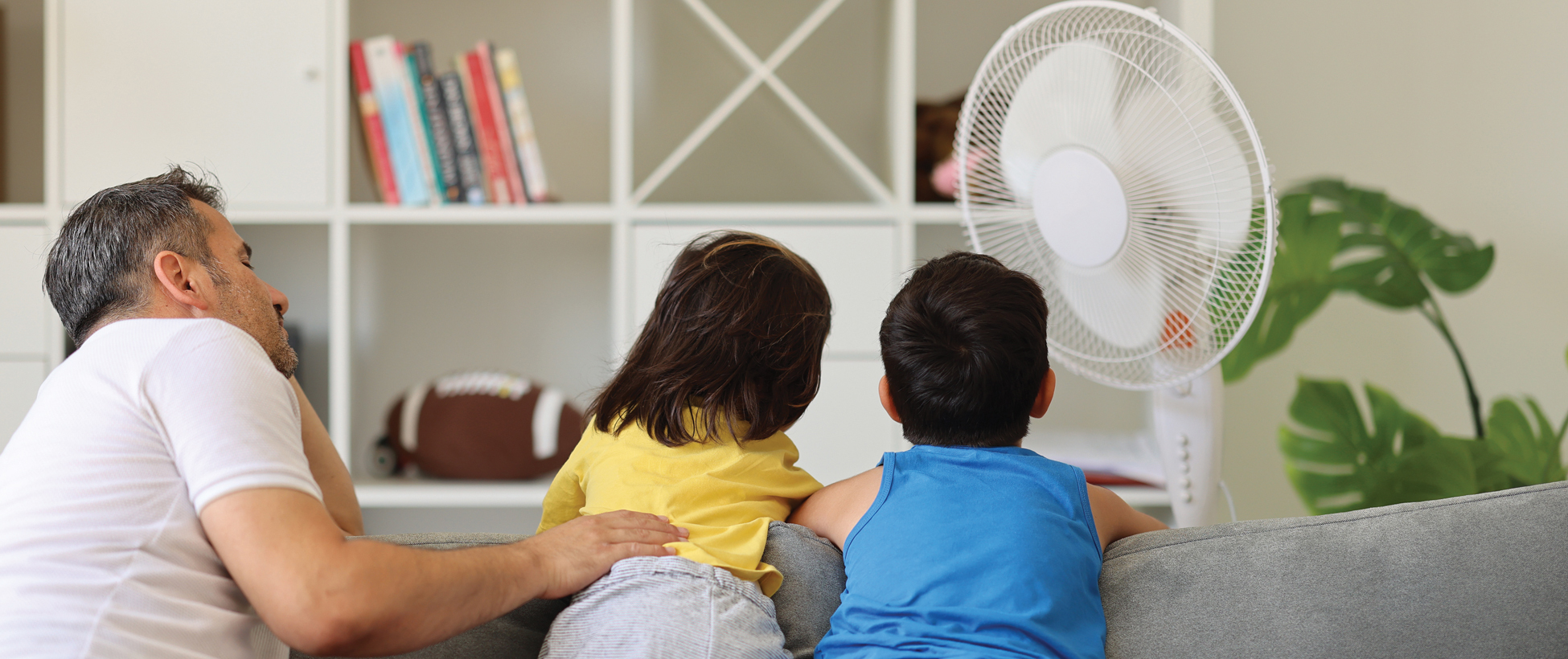 Family relaxing inside beside a fan to help stay cool.