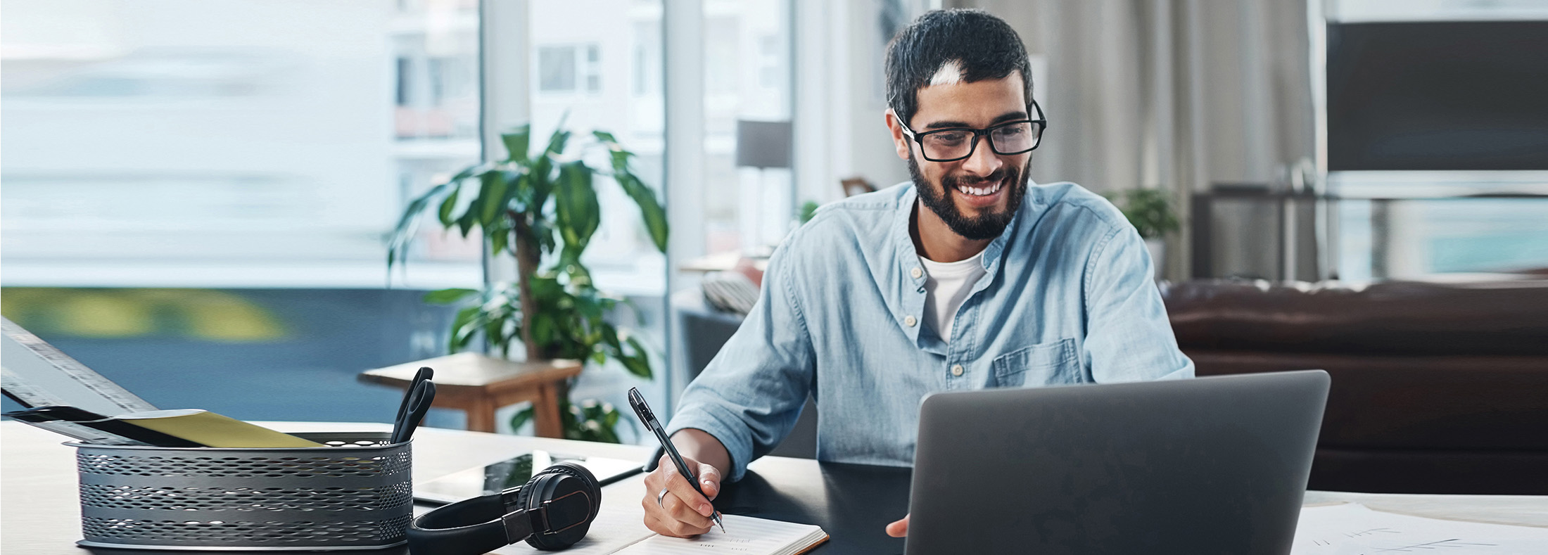 Man sitting at an office desk with a laptop and notepad.'