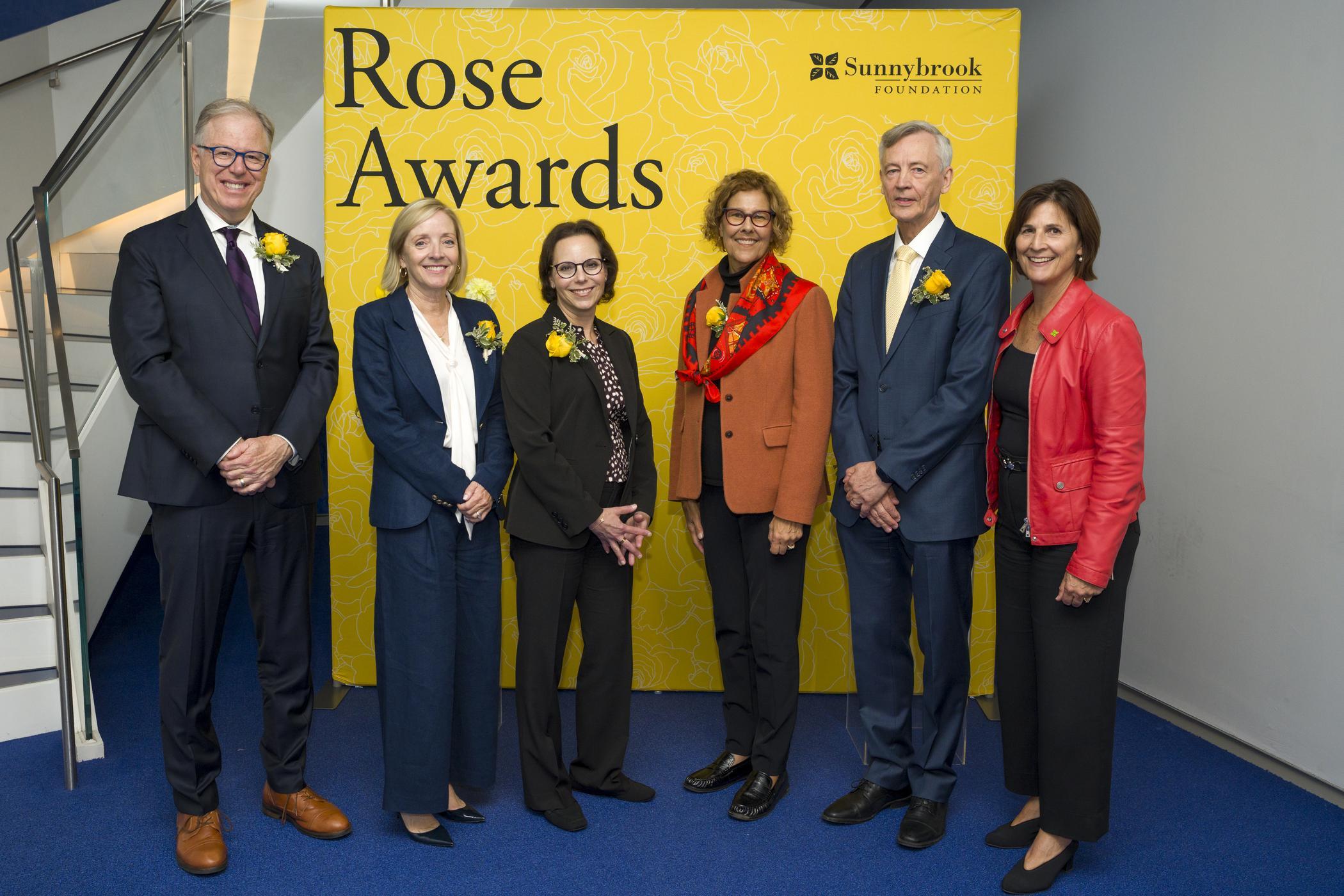 A group of people pose together in front of a backdrop following the Rose Awards presentation.
